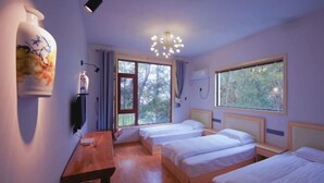 Une chambre avec deux lits, une table en bois, un luminaire fixé au mur et une fenêtre donnant sur des arbres.