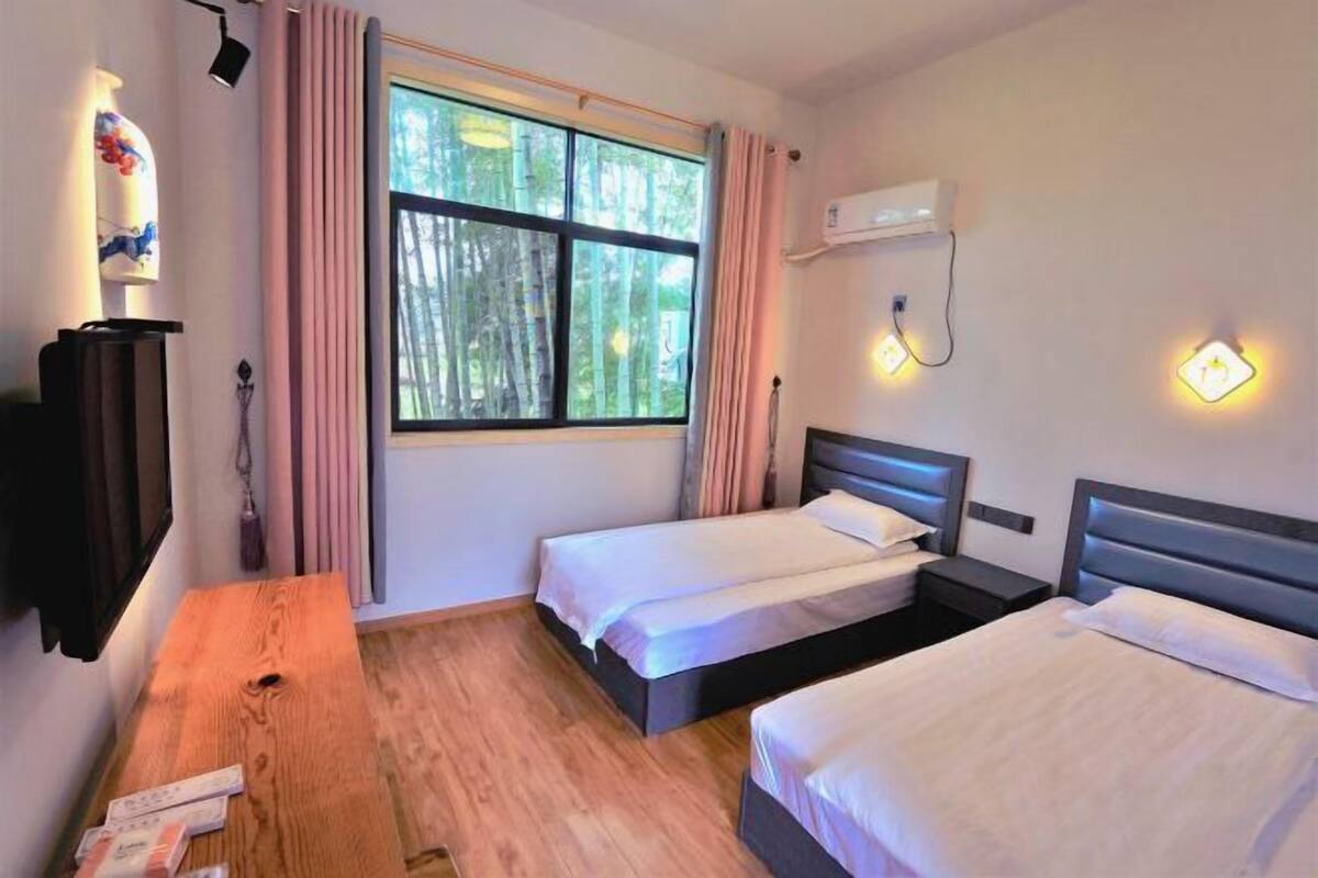 Une chambre avec deux lits, une table en bois, une fenêtre avec des rideaux, un climatiseur et des lampes fixées au mur.