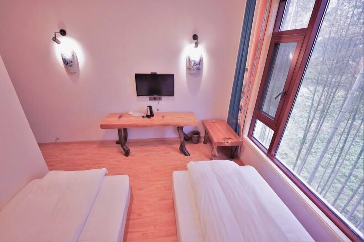 Une chambre avec deux lits, un bureau en bois, une télévision et une fenêtre donnant sur la forêt.