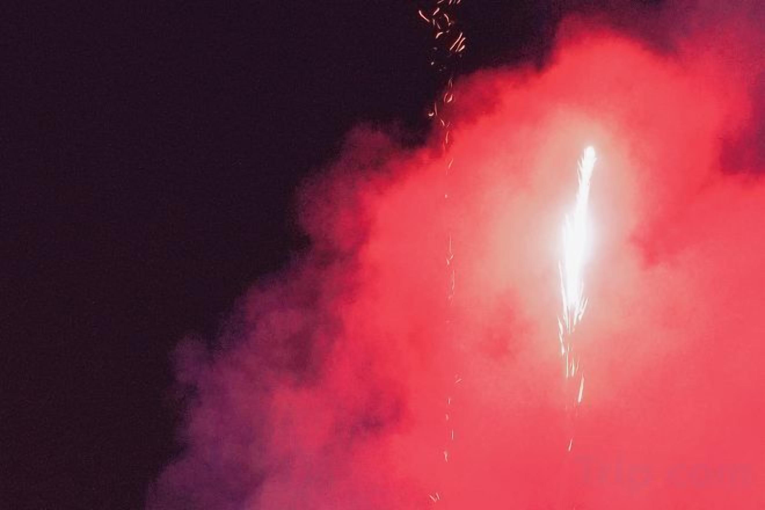 Ein Feuerwerk mit hellem Licht und rotem Rauch vor dunklem Hintergrund.
