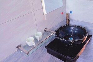 Une salle de bain moderne avec un lavabo noir, une étagère en verre sur laquelle reposent deux tasses blanches et un miroir au mur.