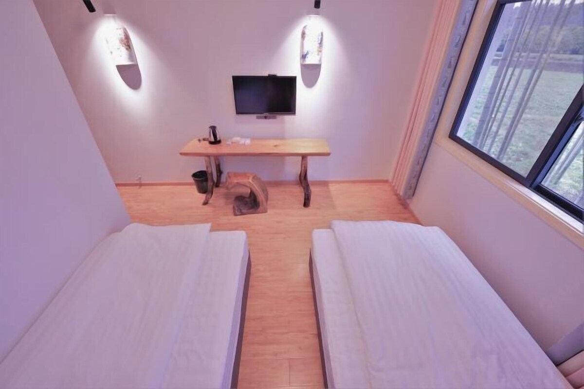 Une chambre avec deux lits, un bureau en bois, une télévision et une fenêtre.