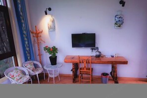 Ein gemütliches Zimmer mit Holztisch, zwei Stühlen, einem Fernseher, einer Topfpflanze und einem kleinen Beistelltisch.