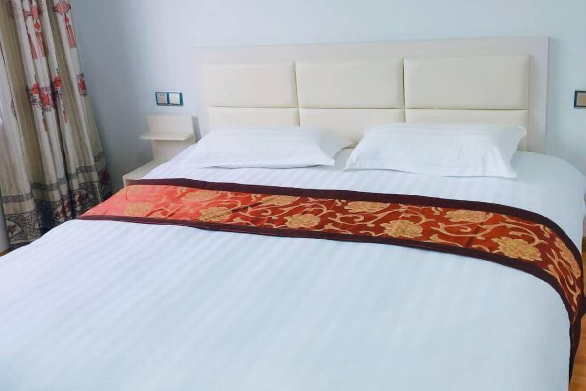 Un lit avec une tête de lit, du linge de lit blanc et un couvre-lit aux motifs rouges et dorés.
