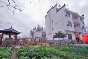 Um edifício tradicional com varanda, cercado por um jardim com plantas e um coreto.