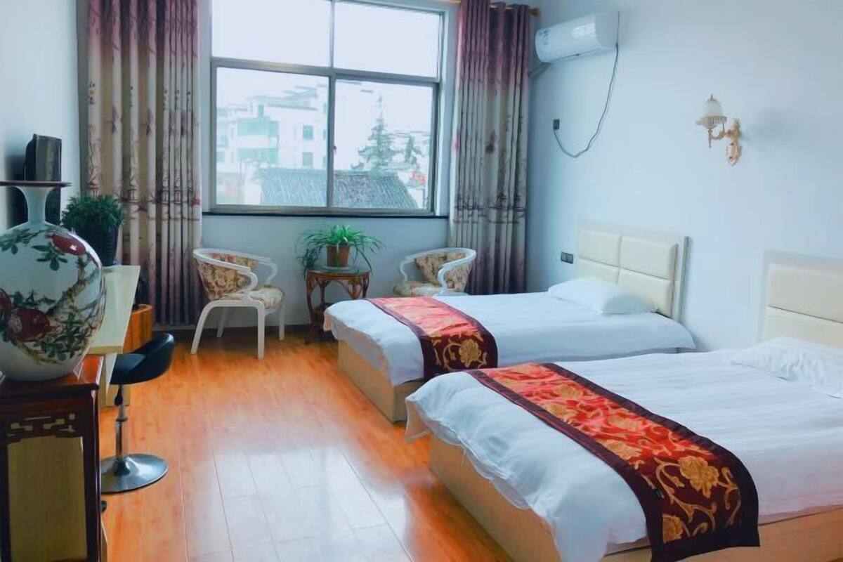 Une chambre d’hôtel avec deux lits, une grande fenêtre, une plante en pot et un vase traditionnel.