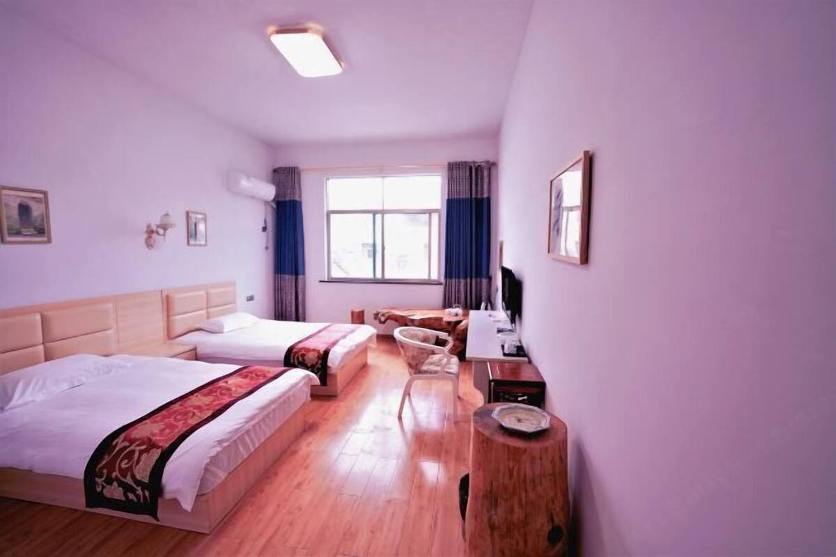 Une chambre d’hôtel avec deux lits, un bureau, une chaise, une fenêtre avec des rideaux et une table d’appoint en bois.