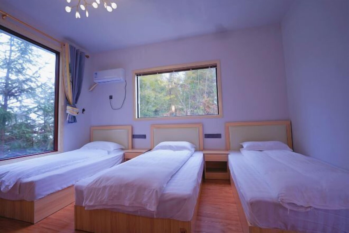 Une chambre avec trois lits simples, une fenêtre donnant sur des arbres et un climatiseur fixé au mur.