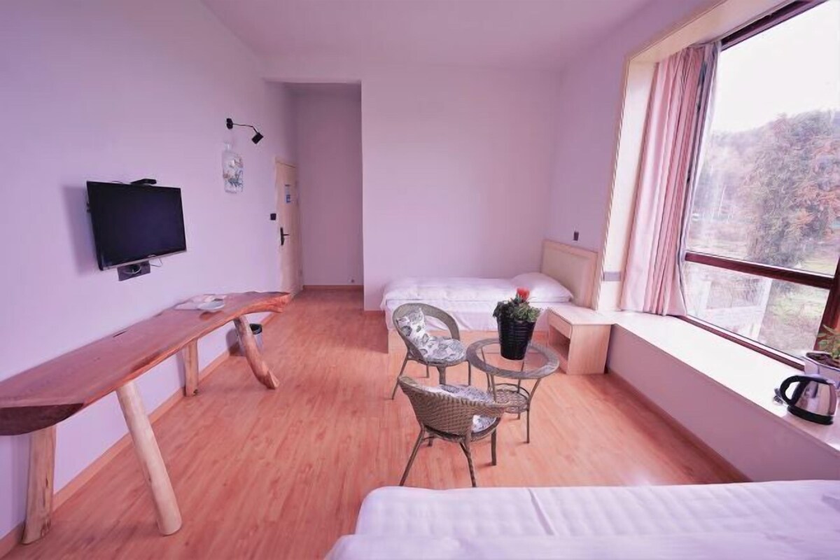 Une chambre avec un lit, un bureau, une chaise, une petite table, un téléviseur et une fenêtre donnant sur un beau paysage.