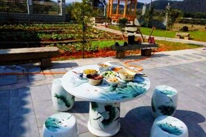 Une table ronde ornée de motifs floraux, entourée de quatre tabourets assortis, est placée sur une terrasse dallée.