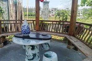 Un belvédère avec une table ronde et un vase, entouré d’une clôture en bois et de verdure.