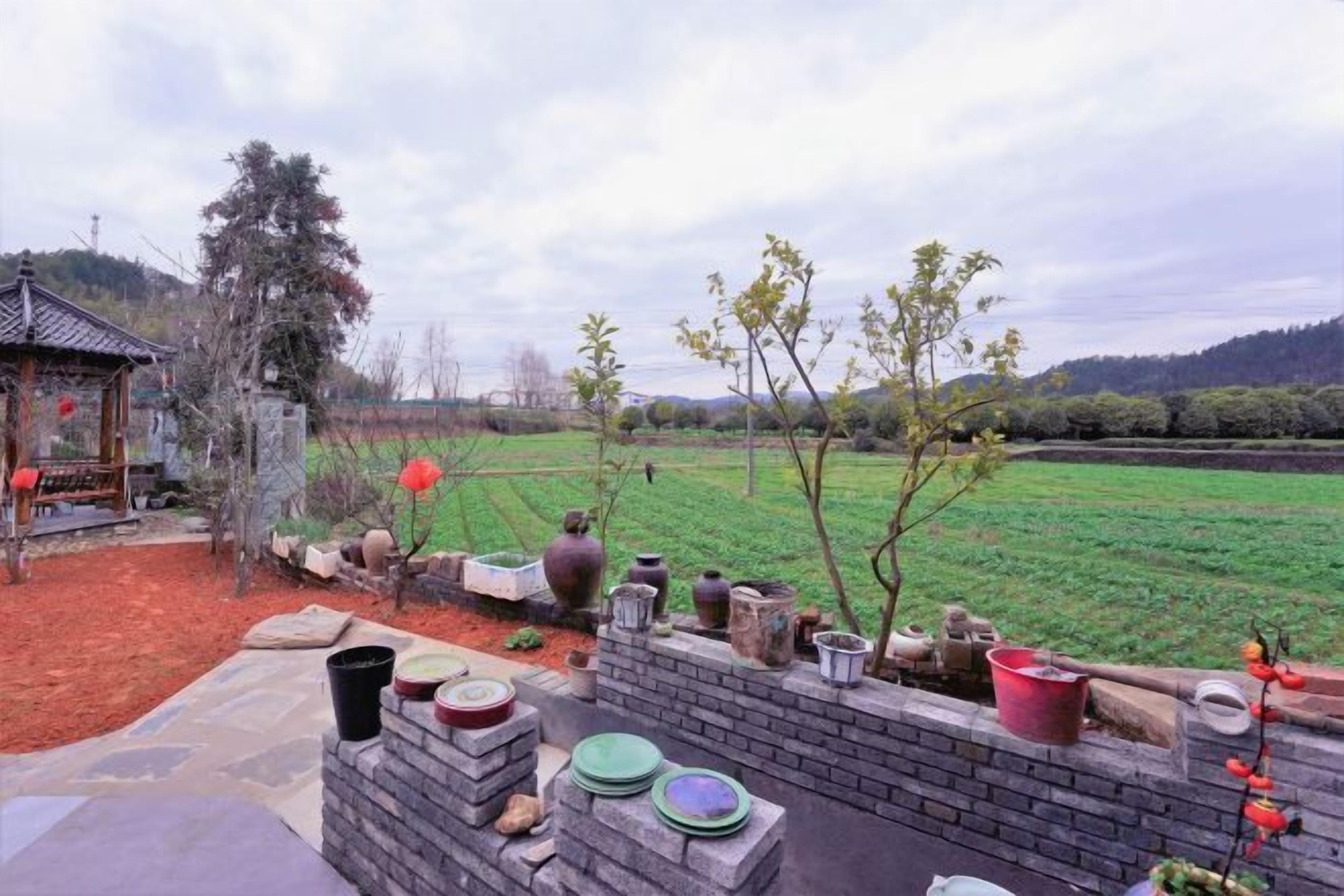Un jardín con muro de ladrillo, diferentes macetas y un pabellón tradicional.