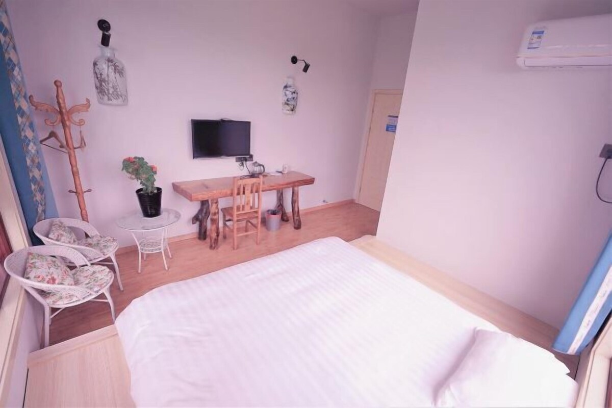 Une chambre à coucher comprenant un lit, un bureau, une chaise, une plante en pot et un téléviseur.