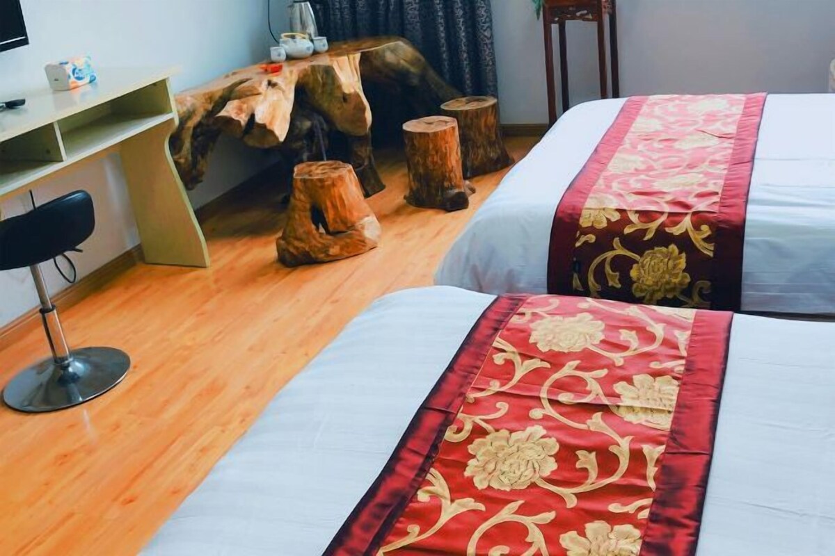 Ein Hotelzimmer mit zwei Betten, einem Schreibtisch und einem Stuhl. Holzstämme und ein Tisch mit Gegenständen darauf sind ebenfalls vorhanden.