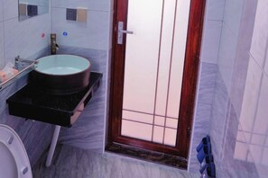 Ein Badezimmer mit rundem Waschbecken, einem Spiegel, einer Toilette und einer Tür mit Gittermuster.
