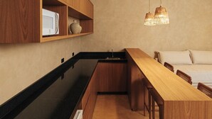 Une cuisine compacte dotée de meubles en bois, d’un plan de travail noir, d’un réfrigérateur encastré et d’un luminaire suspendu.