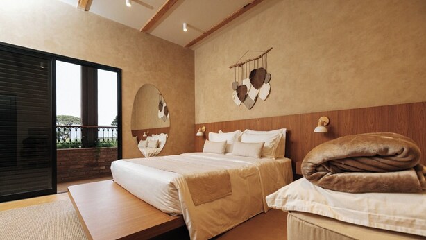 Une chambre avec deux lits, une grande fenêtre, un plafond en bois et une vue sur l’extérieur.