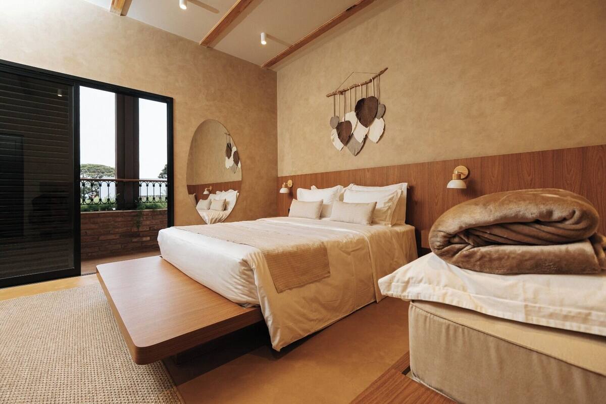 Ein Schlafzimmer mit zwei Betten, einem großen Fenster, einer Holzbalkendecke und Blick ins Freie.
