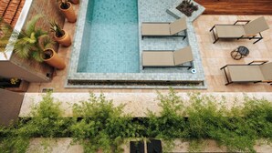 Une piscine extérieure avec un revêtement de carrelage, entourée de chaises longues et de plantes en pot.