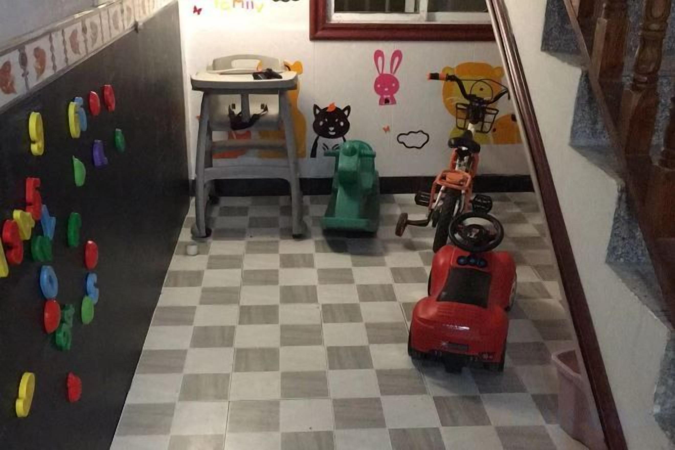 Espaço infantil com um carrinho de brinquedo, um objeto verde e uma parede com letras coloridas.