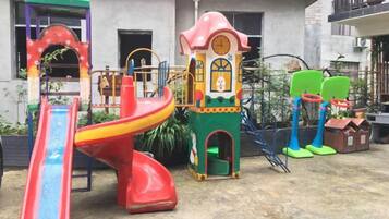 A playground with a red slide, a climbing structure, and a green tower with a clock.