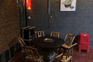 A round table with chairs, a red stool, a wall-mounted light, and a framed picture.