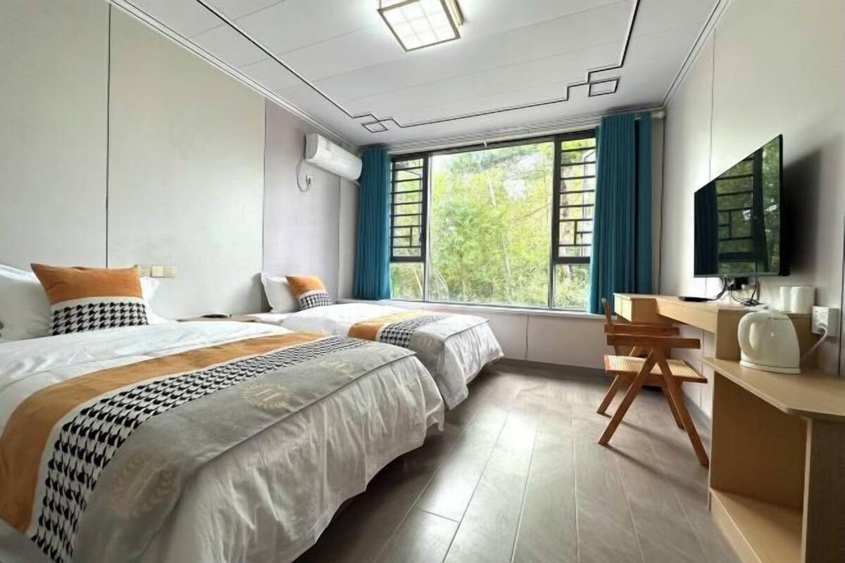 A hotel room with two beds, a desk, a chair, a TV, and a window with curtains.