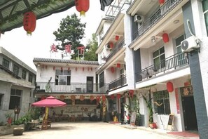 A courtyard with traditional architecture, including a balcony, potted plants, and a red umbrella.