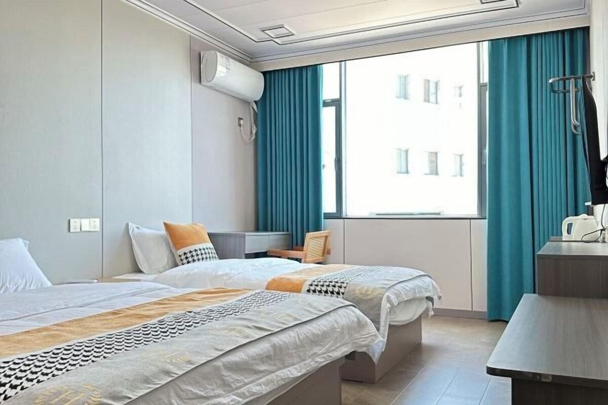A hotel room with two beds, a desk, a chair, and a window with curtains.