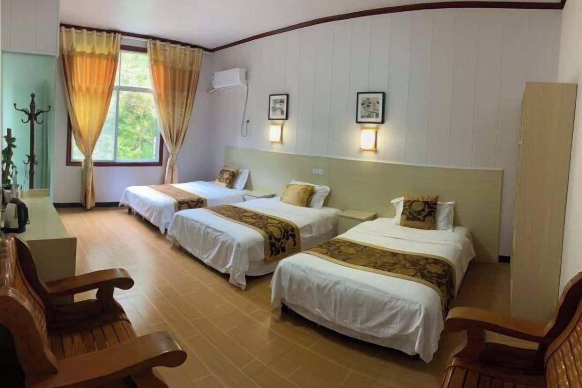 A hotel room with two single beds, a wooden bench, a desk, and a window with curtains.