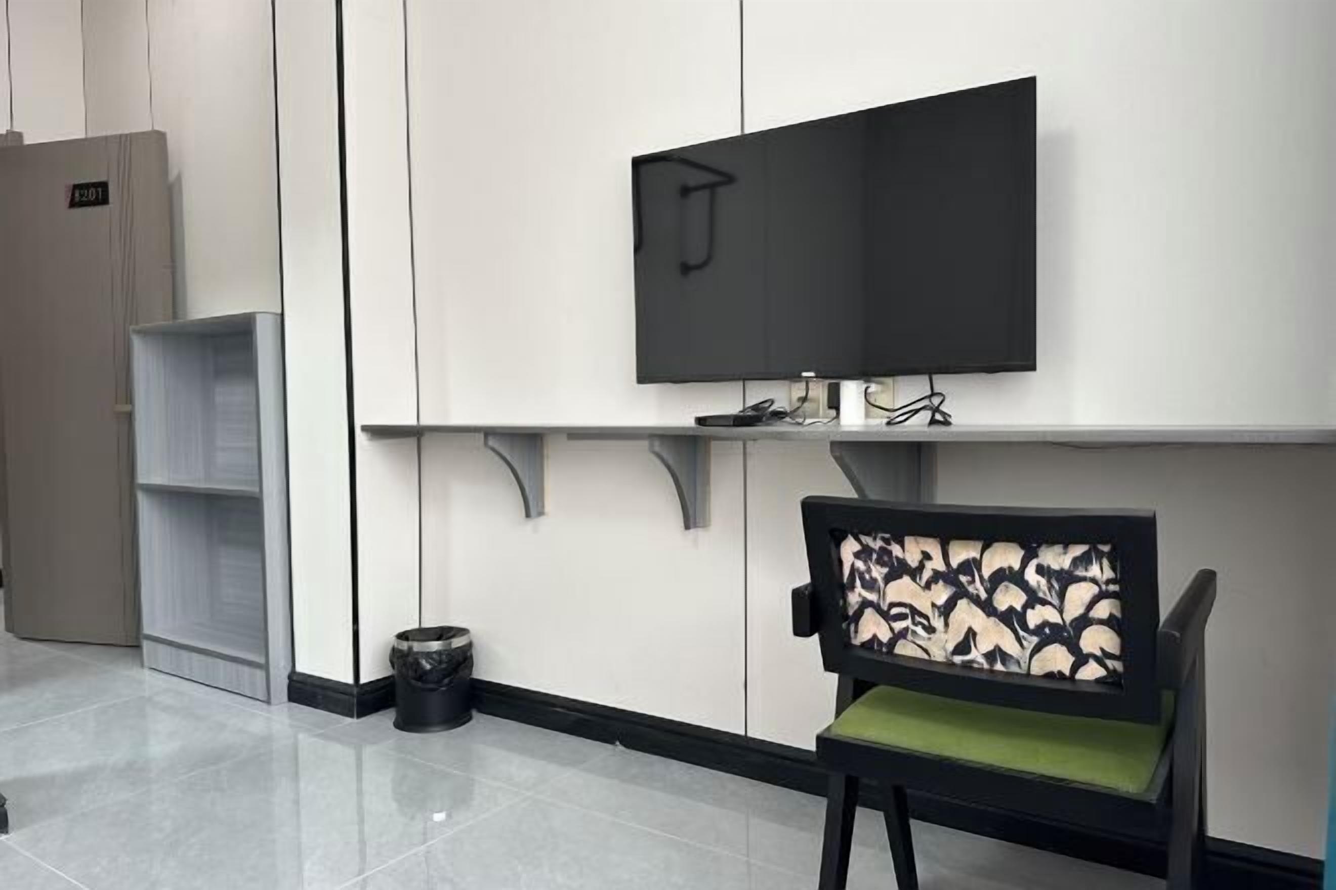 A modern waiting area with a flat-screen TV mounted on the wall, a chair with a patterned backrest, and a trash bin.