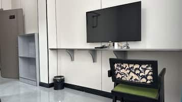 A modern waiting area with a flat-screen TV mounted on the wall, a chair with a patterned backrest, and a trash bin.