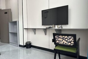 A modern waiting area with a flat-screen TV mounted on the wall, a chair with a patterned backrest, and a trash bin. - Bodaofeng Donglixia Farmhouse (Luotian County)