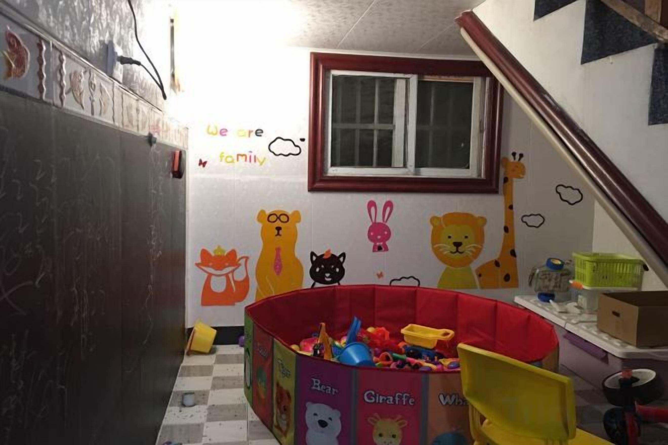 Un'area giochi per bambini con un recinto rosso, giocattoli e decorazioni murali con personaggi di animali.