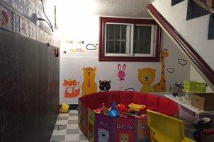 Zona de juegos para niños con una jaula roja, juguetes y decoraciones en la pared que incluyen personajes de animales.