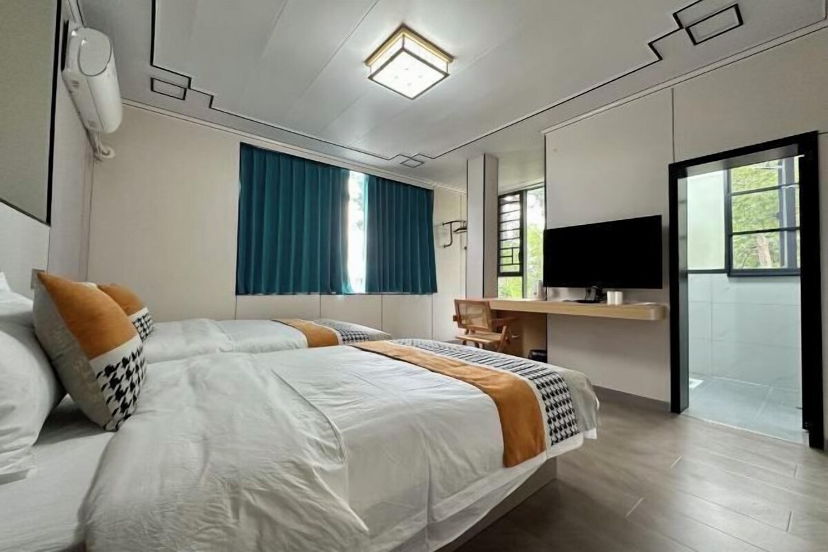 A modern hotel room with a large bed, a desk, a television, and a window with curtains.
