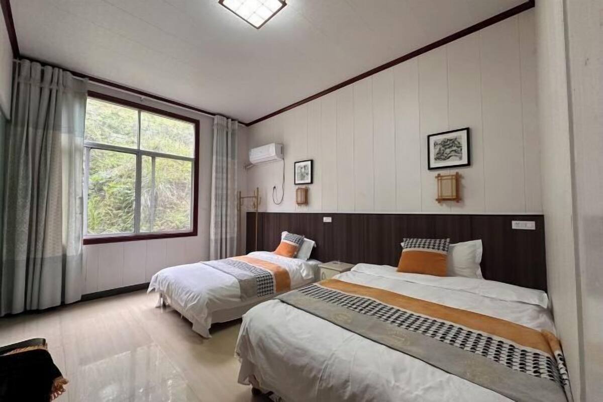 A hotel room with two beds, a large window with curtains, an air conditioning unit, and a framed picture on the wall.