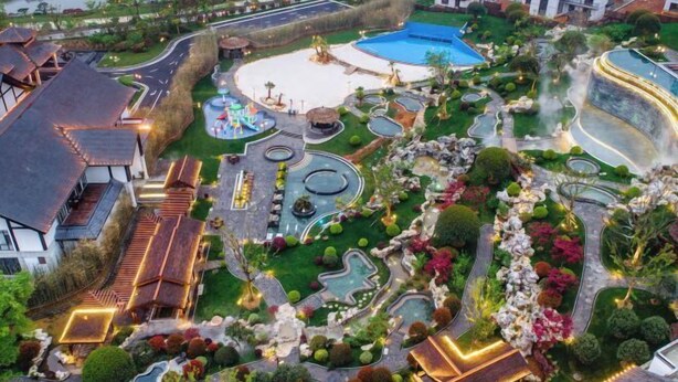 Vue aérienne d’un complexe hôtelier avec des allées sinueuses, une piscine centrale et des jardins aménagés.