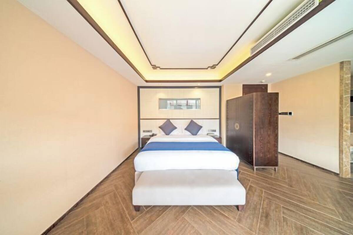 Quarto de hotel moderno com uma cama grande, uma mesa de cabeceira, um guarda-roupa e iluminação embutida no teto.