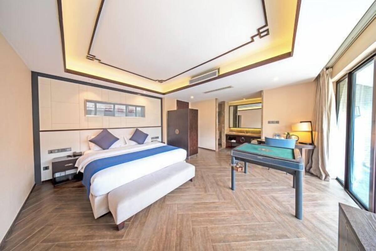 Quarto de hotel moderno com uma cama grande, mesa de bilhar e uma janela ampla.