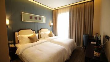 Quarto de hotel com duas camas, uma mesa de trabalho, uma cadeira, uma luminária e uma janela com cortinas.