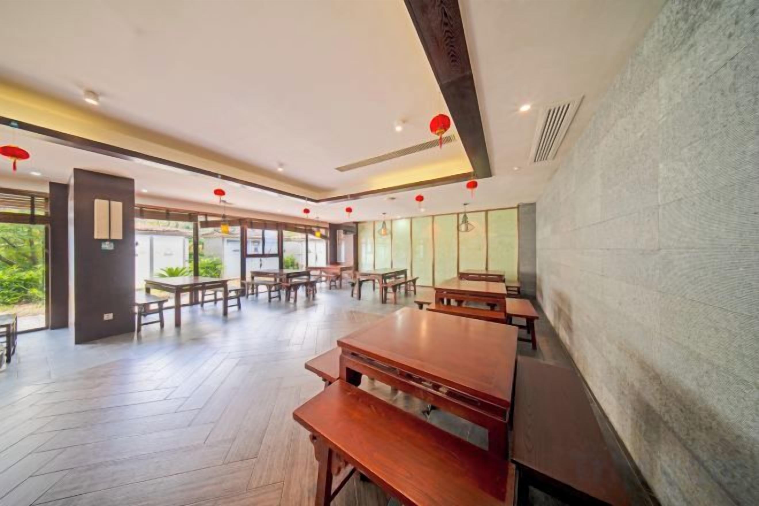 A spacious indoor area with wooden tables and benches, large windows, and a stone wall.