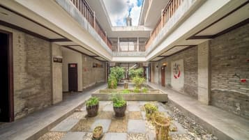 Une cour intérieure avec un jardin central, de nombreuses portes et un plafond haut doté de lucarnes.