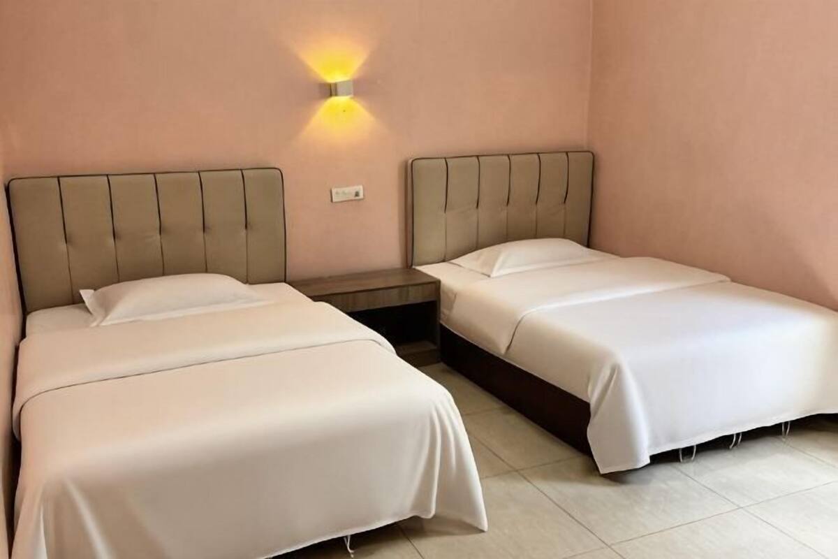 Una habitación con dos camas, una mesita de noche y una lámpara fijada a la pared.