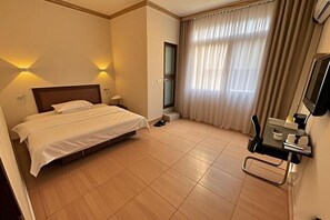 A hotel room with a bed, a desk with a chair, a TV, and a window with curtains. - hongdu hotel (Laibin)