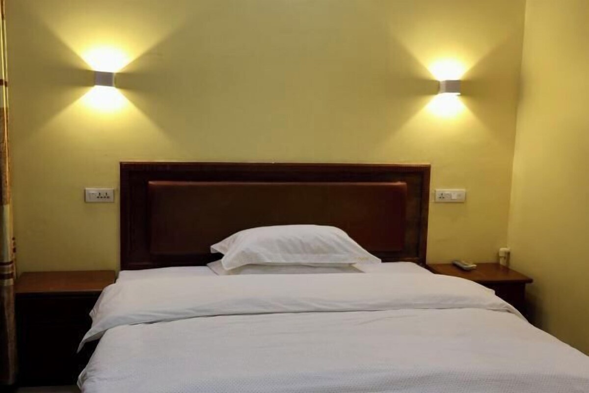 Une chambre d’hôtel avec une tête de lit en bois, deux tables de chevet et deux lampes fixées au mur.