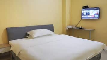 A neatly made bed with white linens in a room with a yellow wall and a flat-screen TV mounted on the wall.