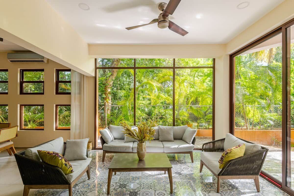 A spacious room with a large window, a ceiling fan, and a sofa set.