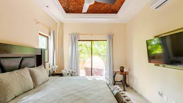 A bedroom with a bed, a ceiling fan, a TV mounted on the wall, and a window with curtains.