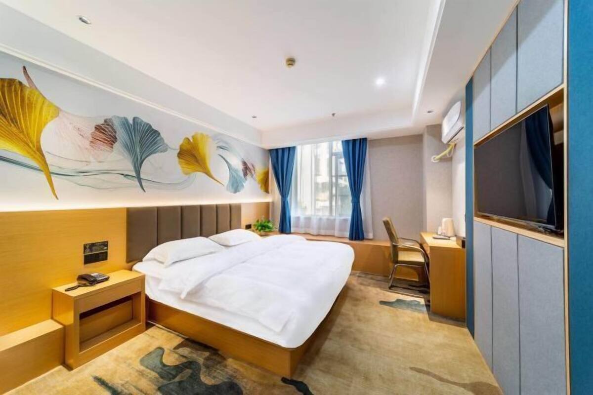 A hotel room with a large bed, a desk, a television, and a decorative wall mural.